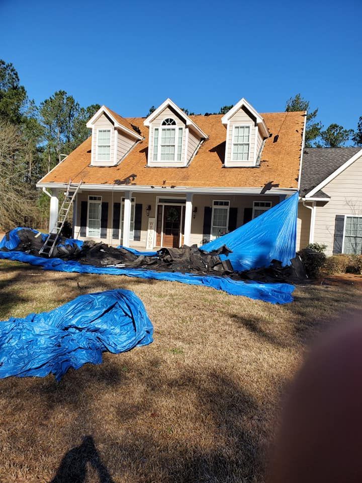 House with a partially replaced roof, blue tarps covering debris on the lawn, and a ladder leaning against the house.