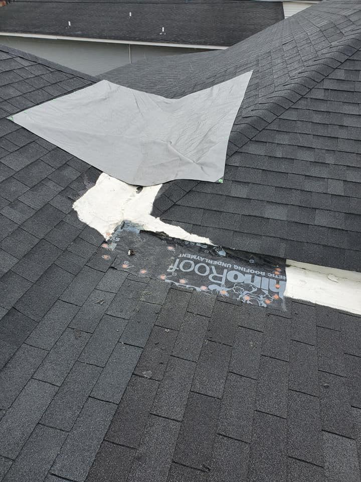 Close-up of a damaged roof with missing shingles and a tarp covering the exposed area. Black asphalt shingles and a white underlayment are visible.