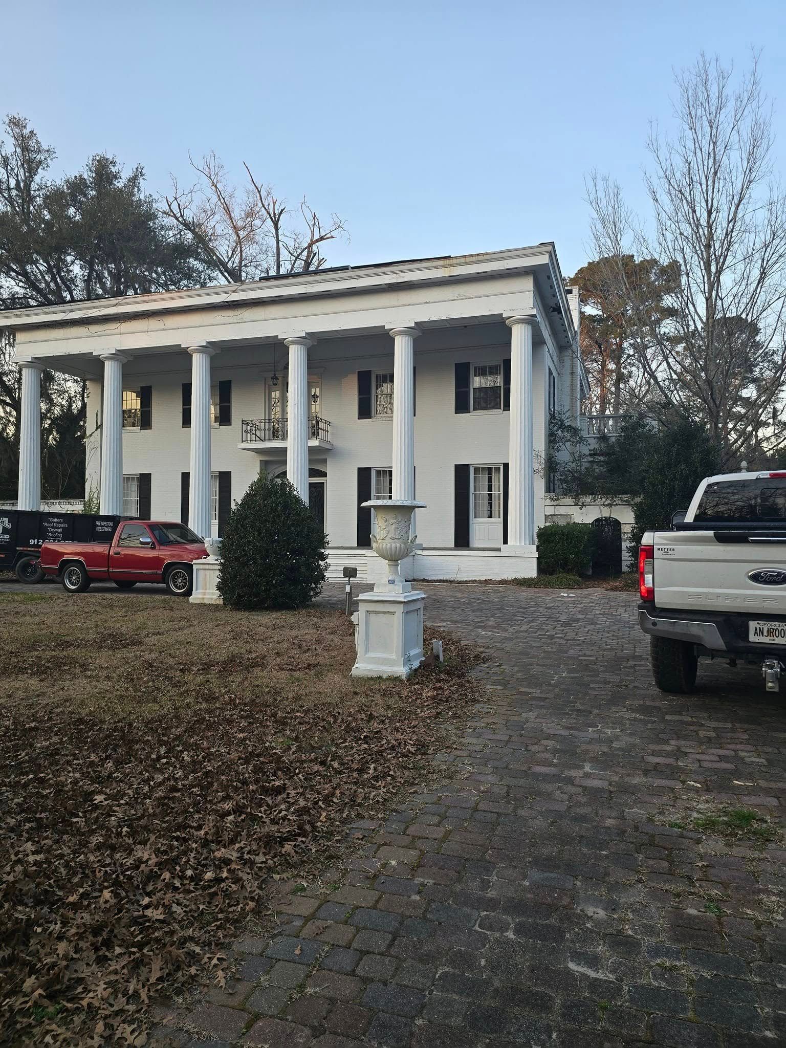 White two-story mansion with large columns. A red pickup truck and white truck are parked in the driveway.