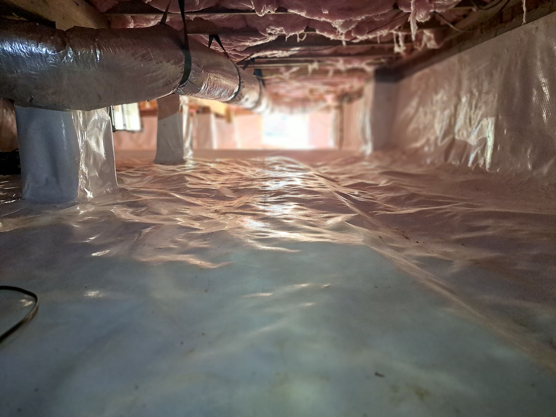 Crawlspace with white plastic vapor barrier on the ground and walls, ductwork, and insulation above.