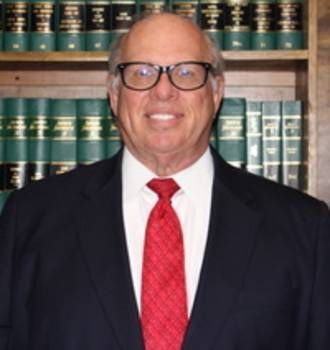 A man in a suit and tie is standing in front of a bookshelf.