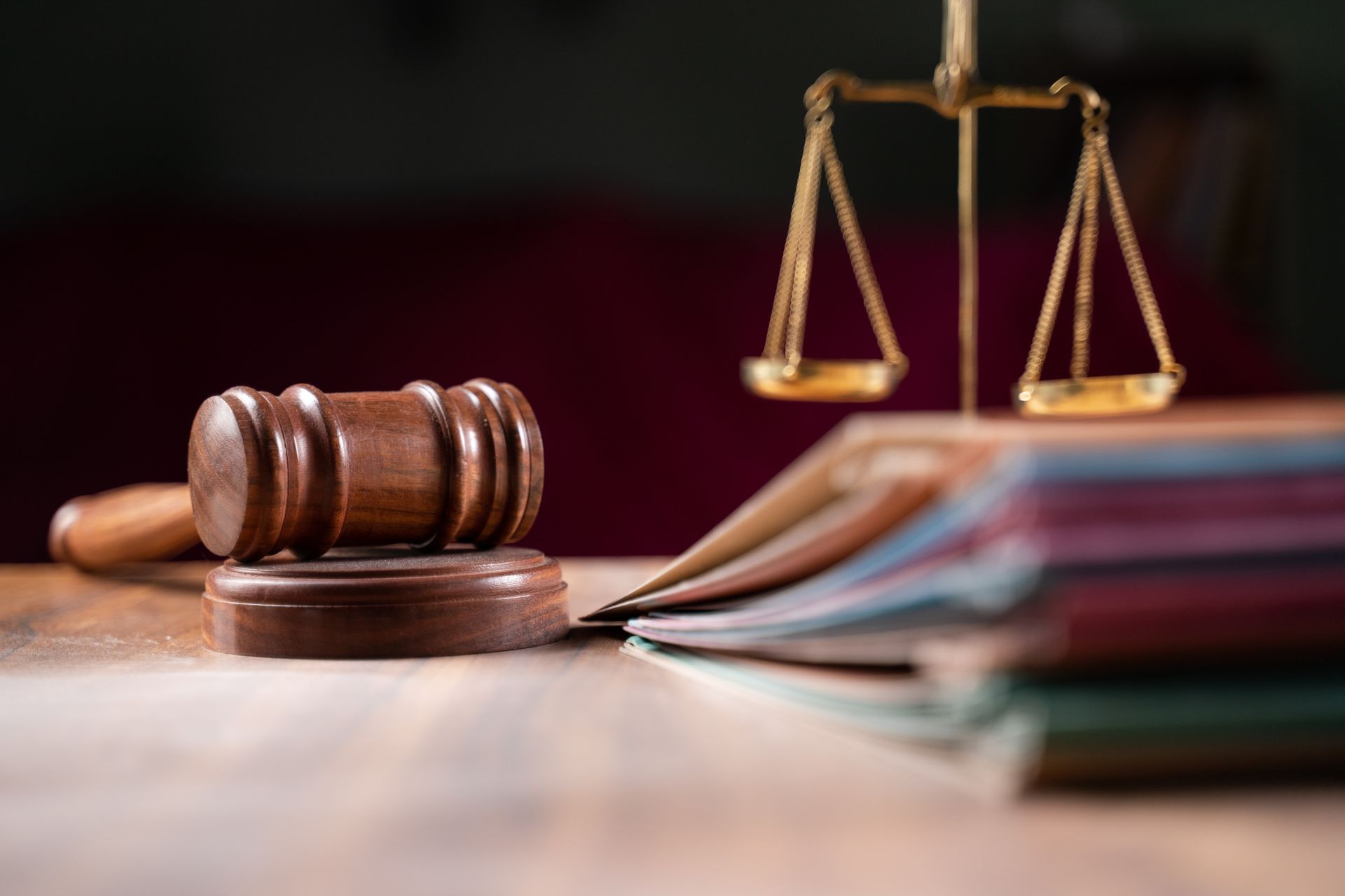 A wooden gavel and scales of justice are on a wooden table.