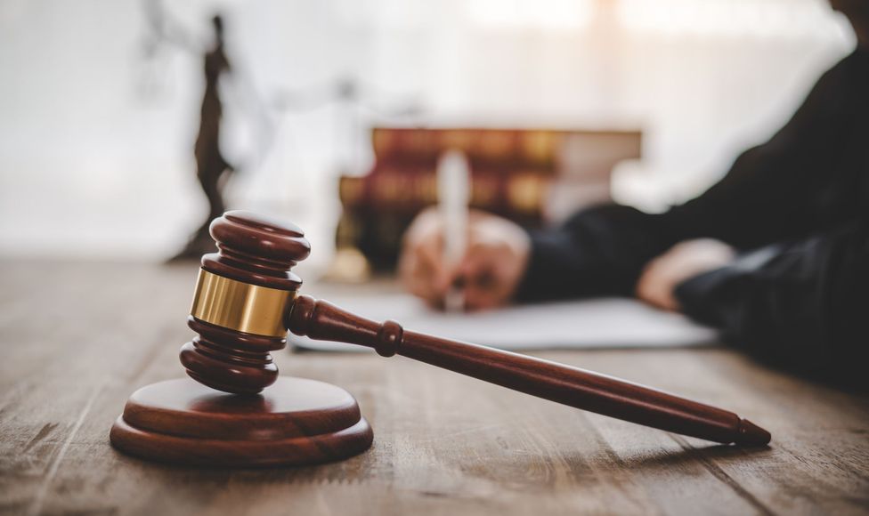 A judge 's gavel is sitting on a wooden table in front of a judge writing on a piece of paper.