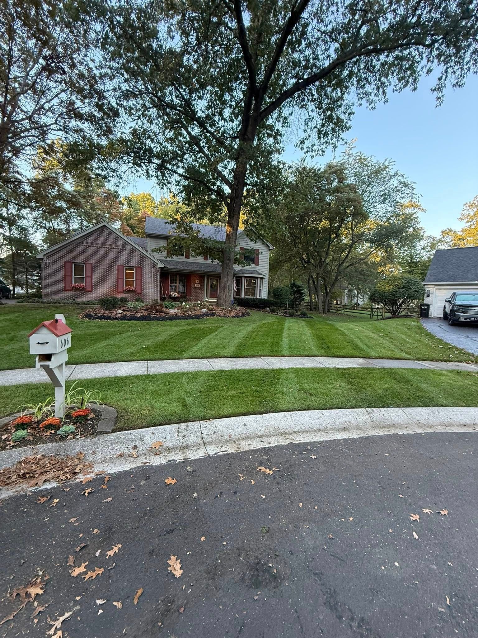 A view from a zero-turn mower cutting grass in a sunny, green backyard with a small playhouse in the distance.