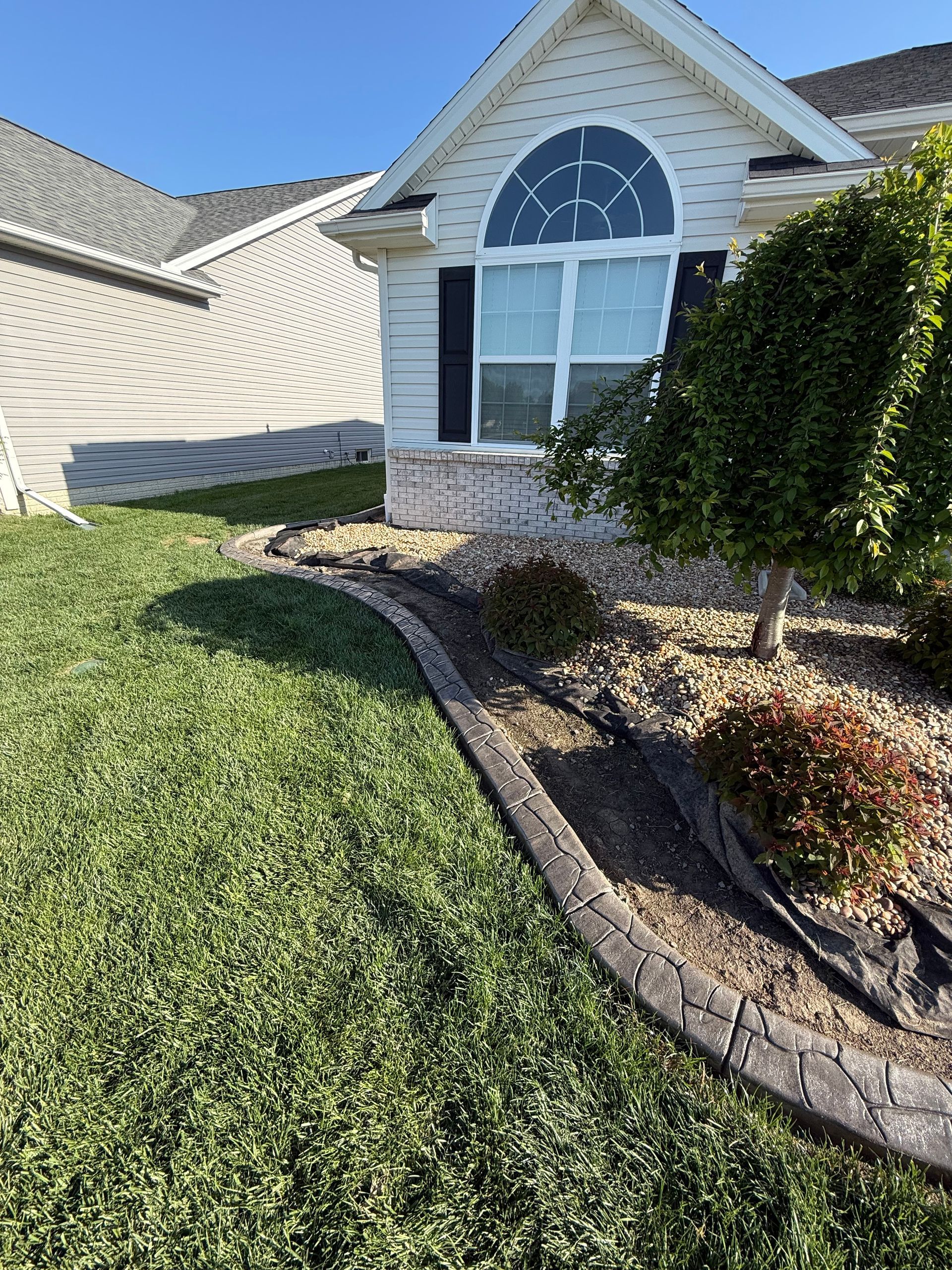 A residential house exterior featuring a curved stone landscape border separating green grass from a gravel garden bed.
