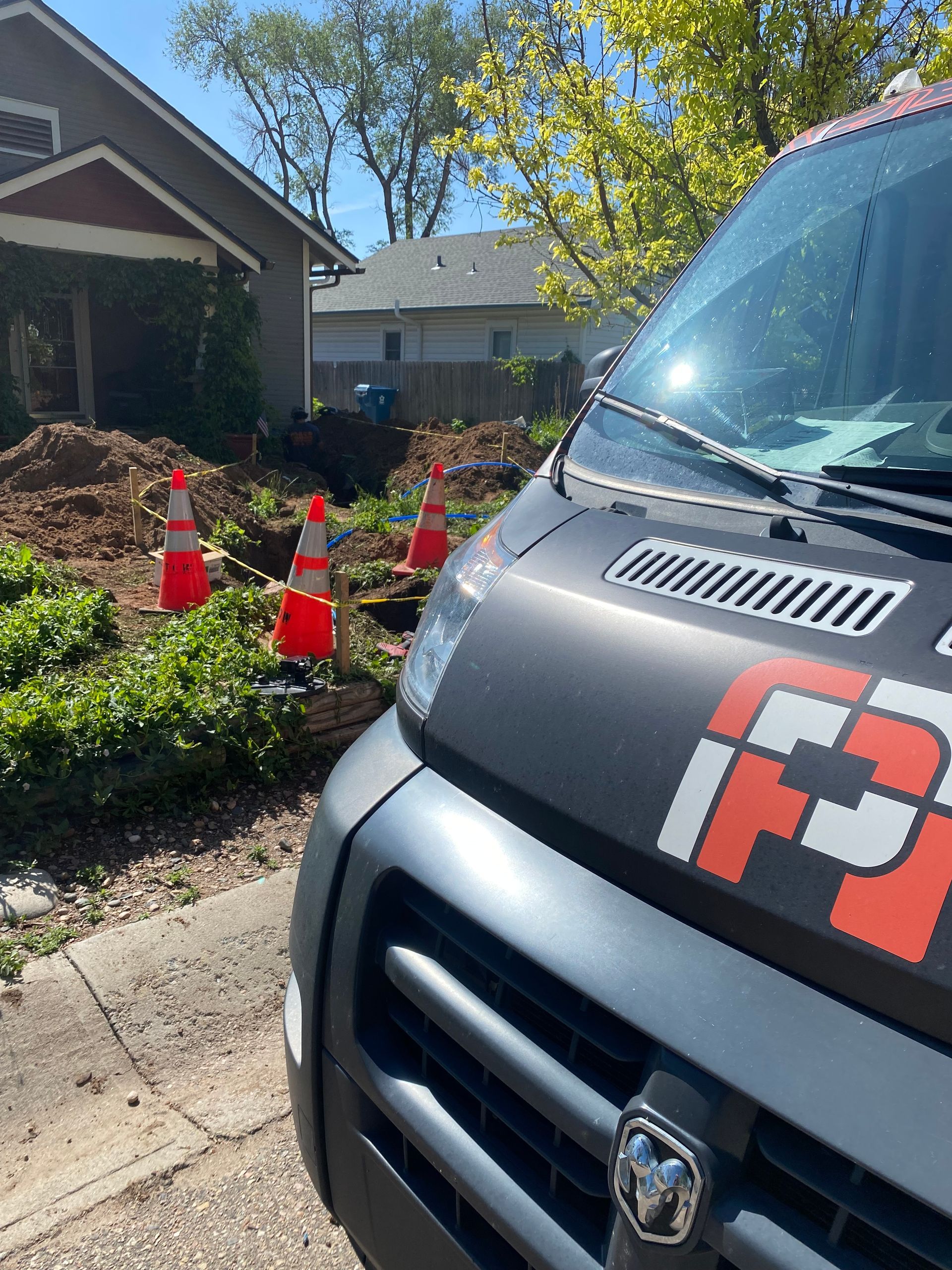 Gray service van parked near a construction site with orange cones and a house in the background.