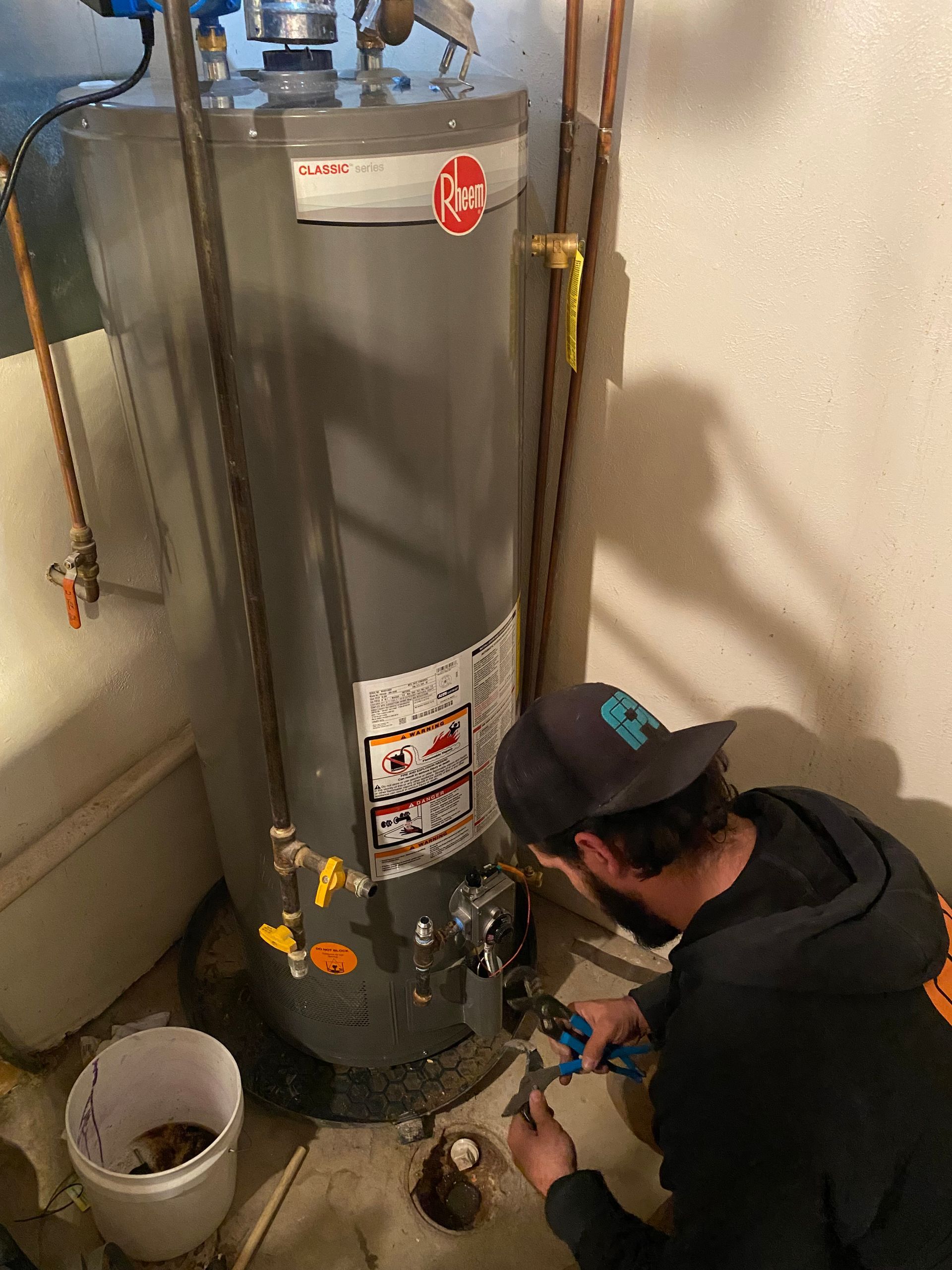A plumber working on a water heater in a basement; they are using a wrench.