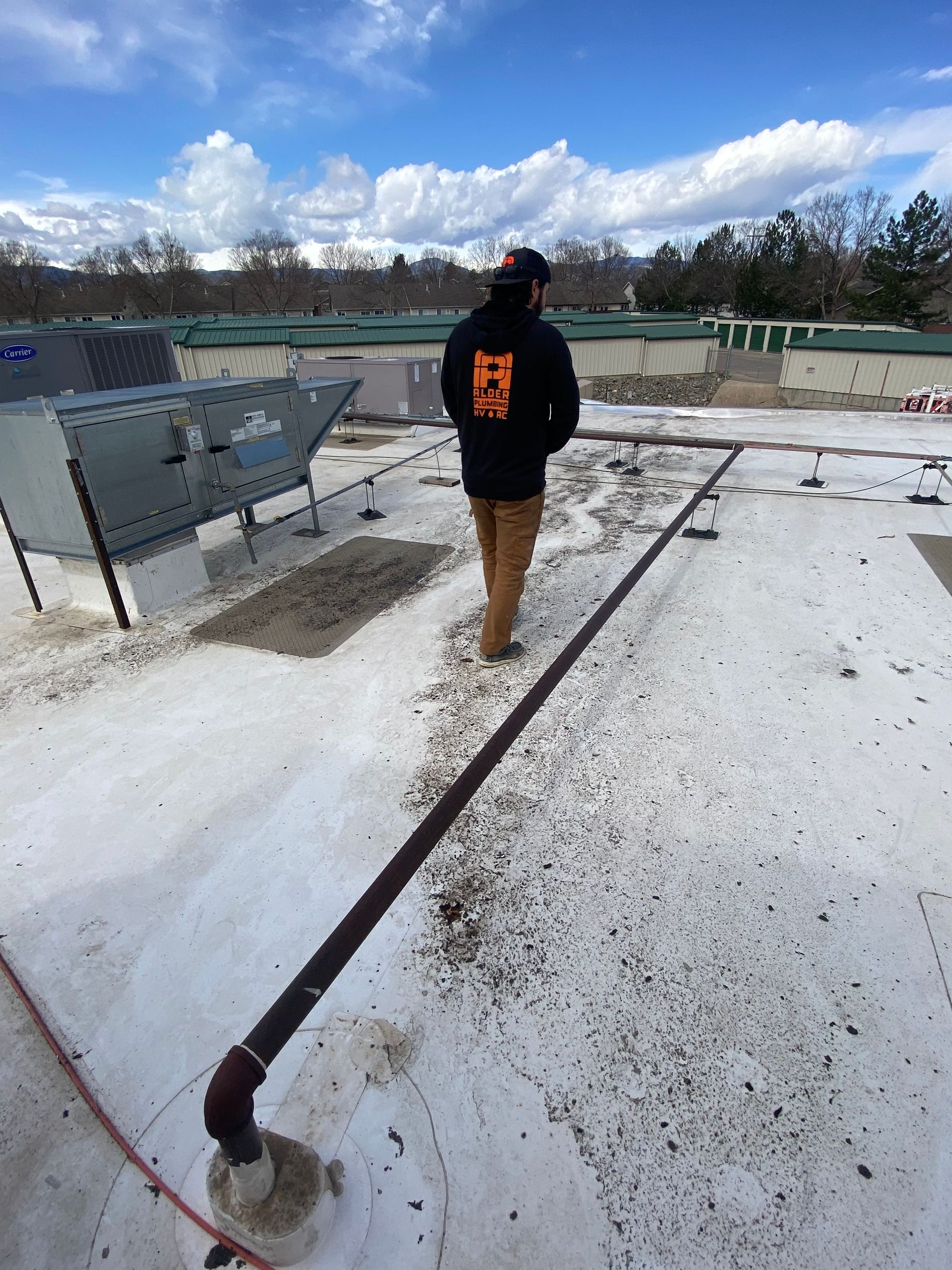 Person on a rooftop, wearing a dark jacket, brown pants. A line of debris runs across the white roof.
