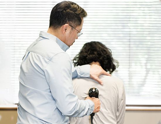 Dr. Alex Oh examining a woman 's back with a stethoscope.