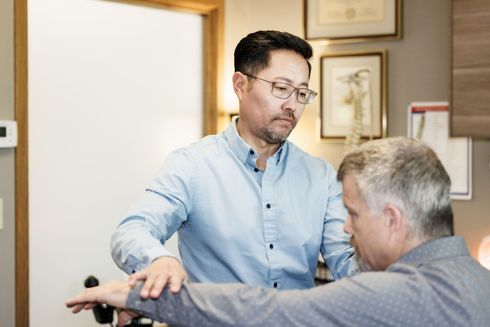 Dr. Alex Oh helping man stretch his arm in a room.
