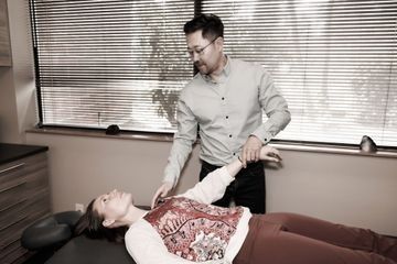 Dr. Alex Oh stretching a woman 's arm in a room.