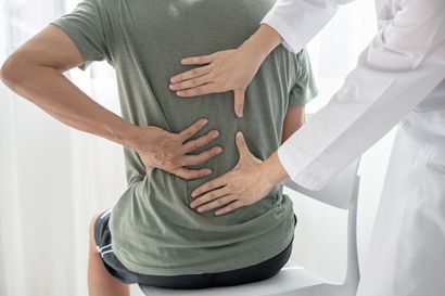 A man is sitting on a chair while a doctor examines his back.