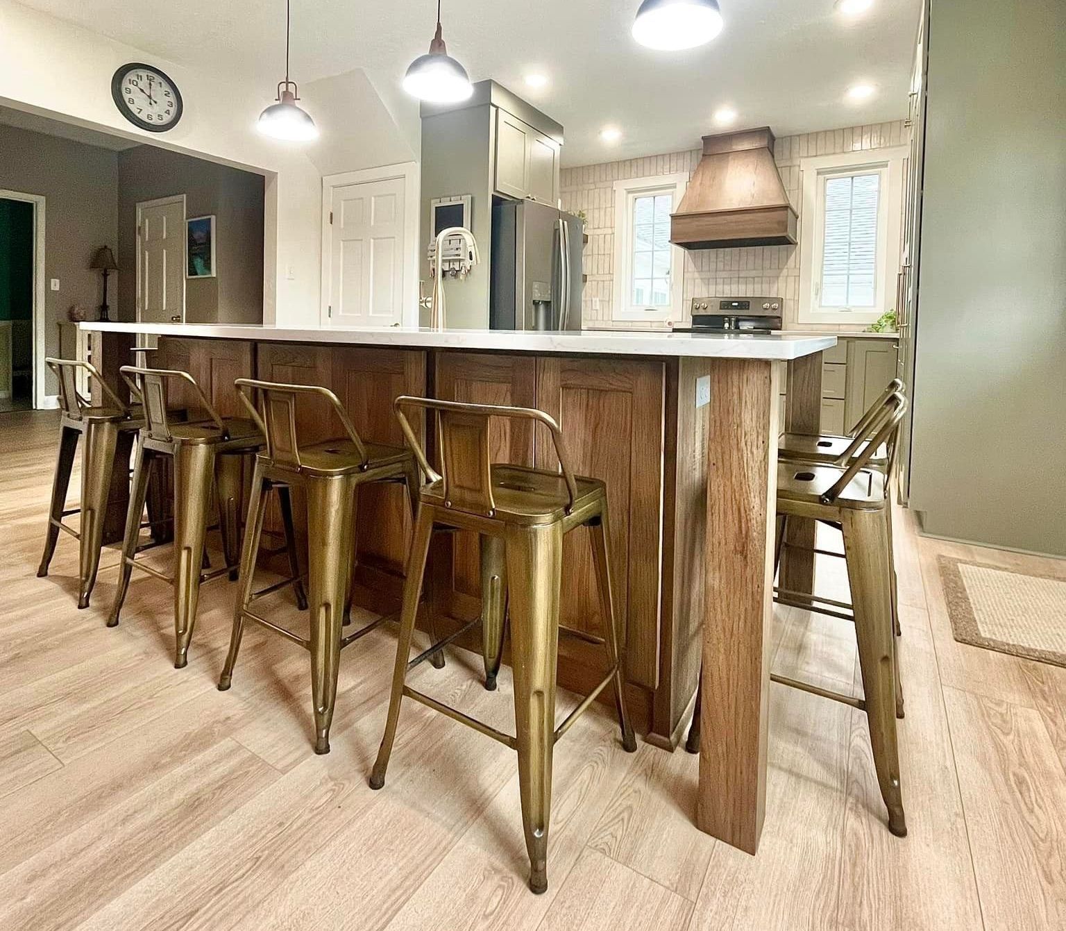 A kitchen with a large island and stools and a clock on the wall.