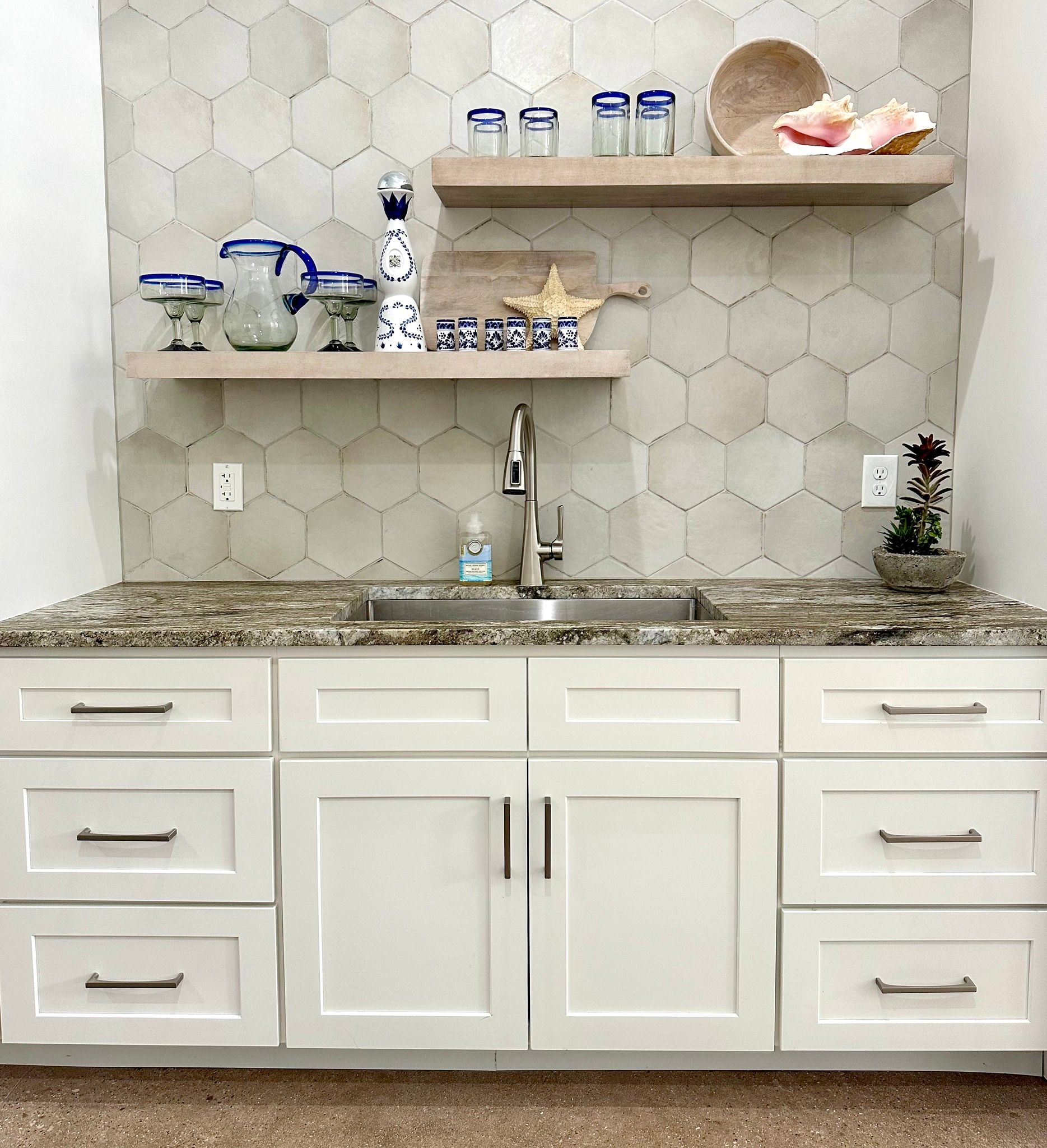 A kitchen with white cabinets , a sink , and a marble counter top.