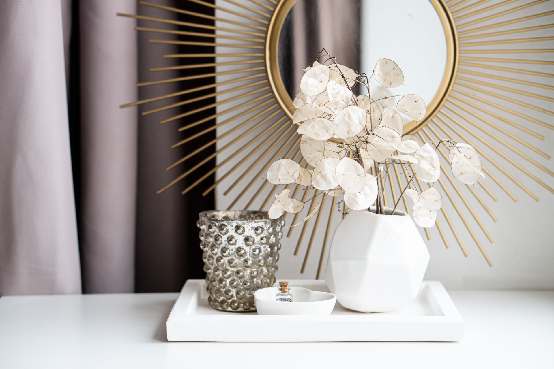 A vase of flowers is sitting on a tray on a table next to a mirror.