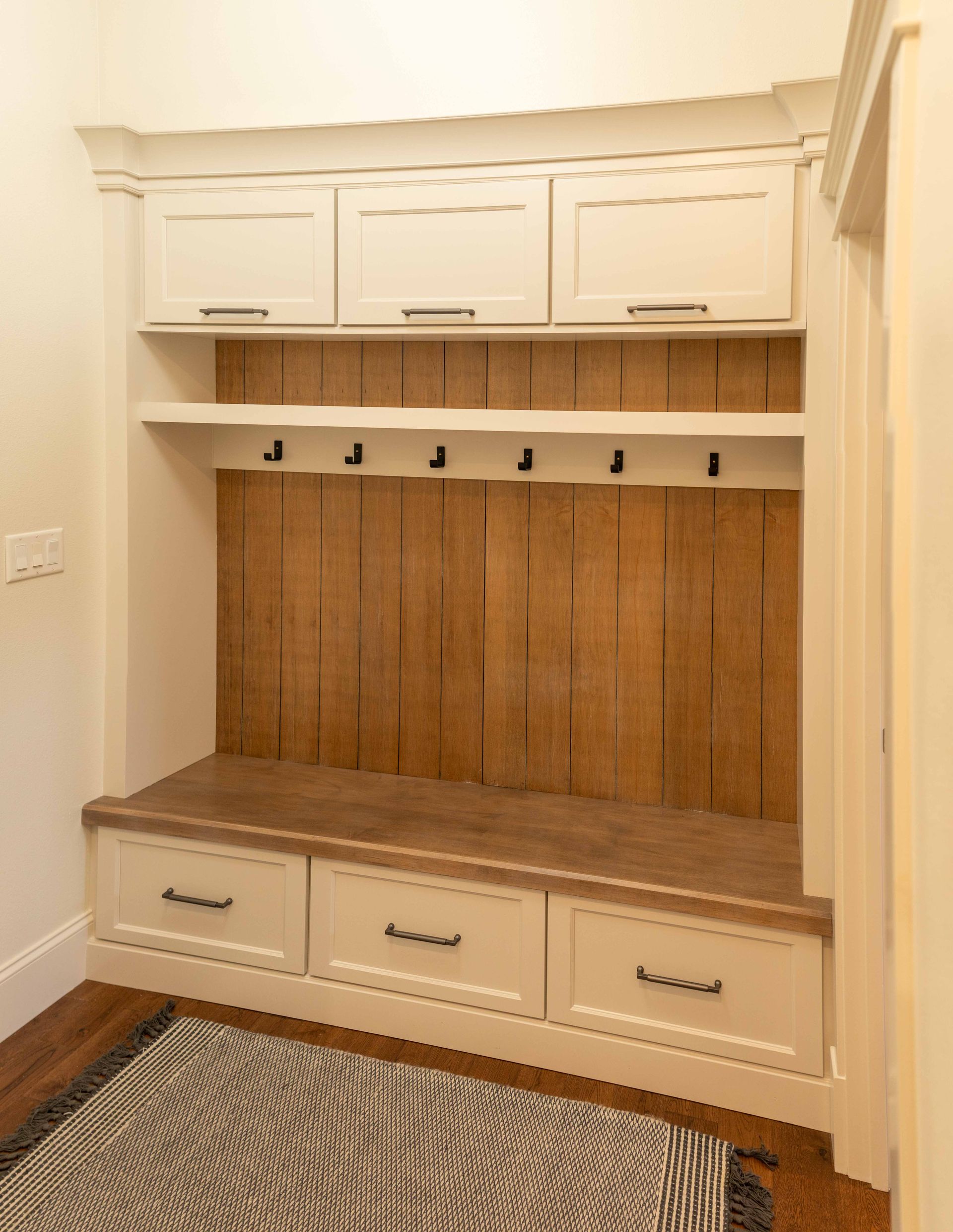 A hallway with a bench , shelves , hooks and drawers.