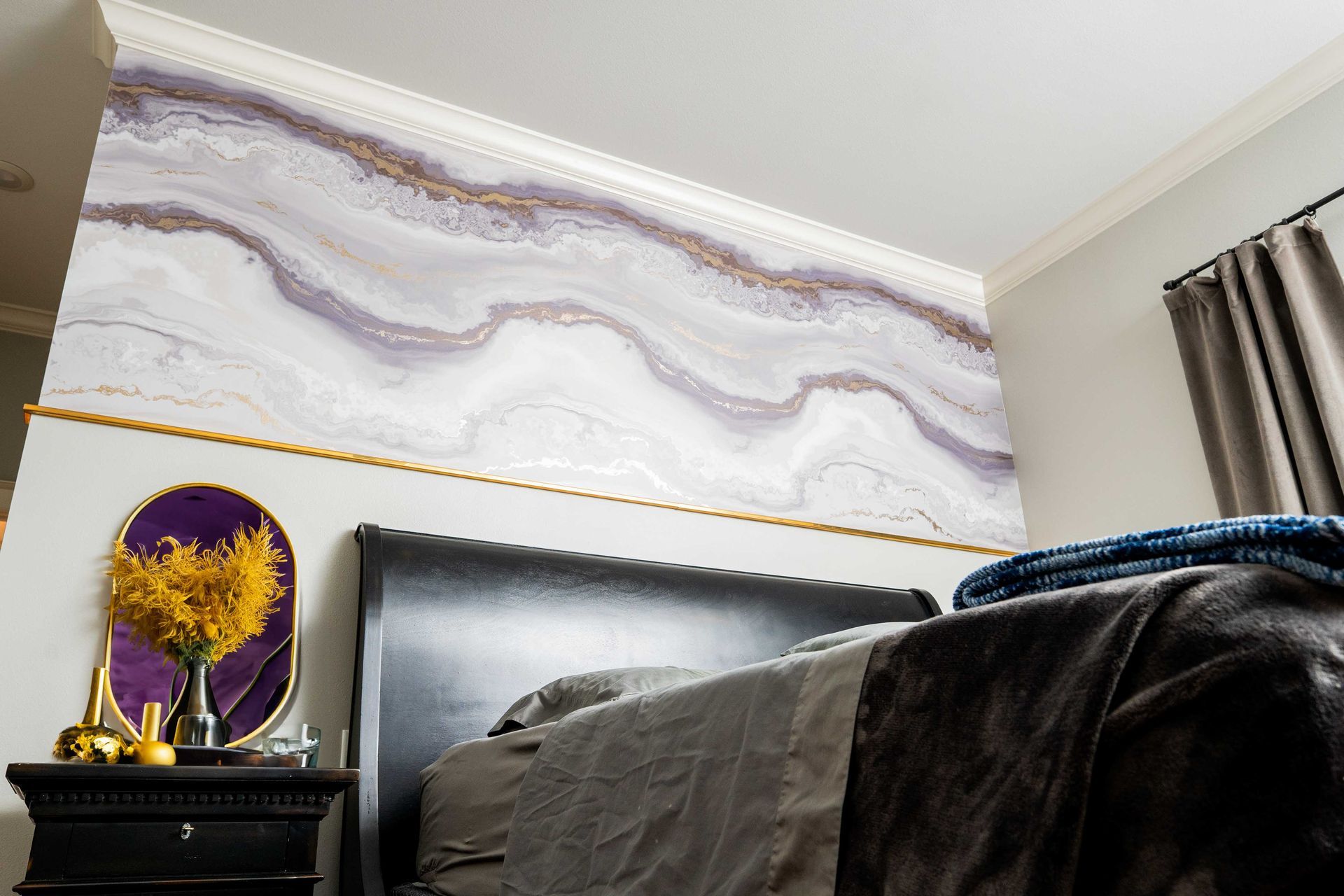 A bedroom with a bed , nightstand , mirror and marble wall.