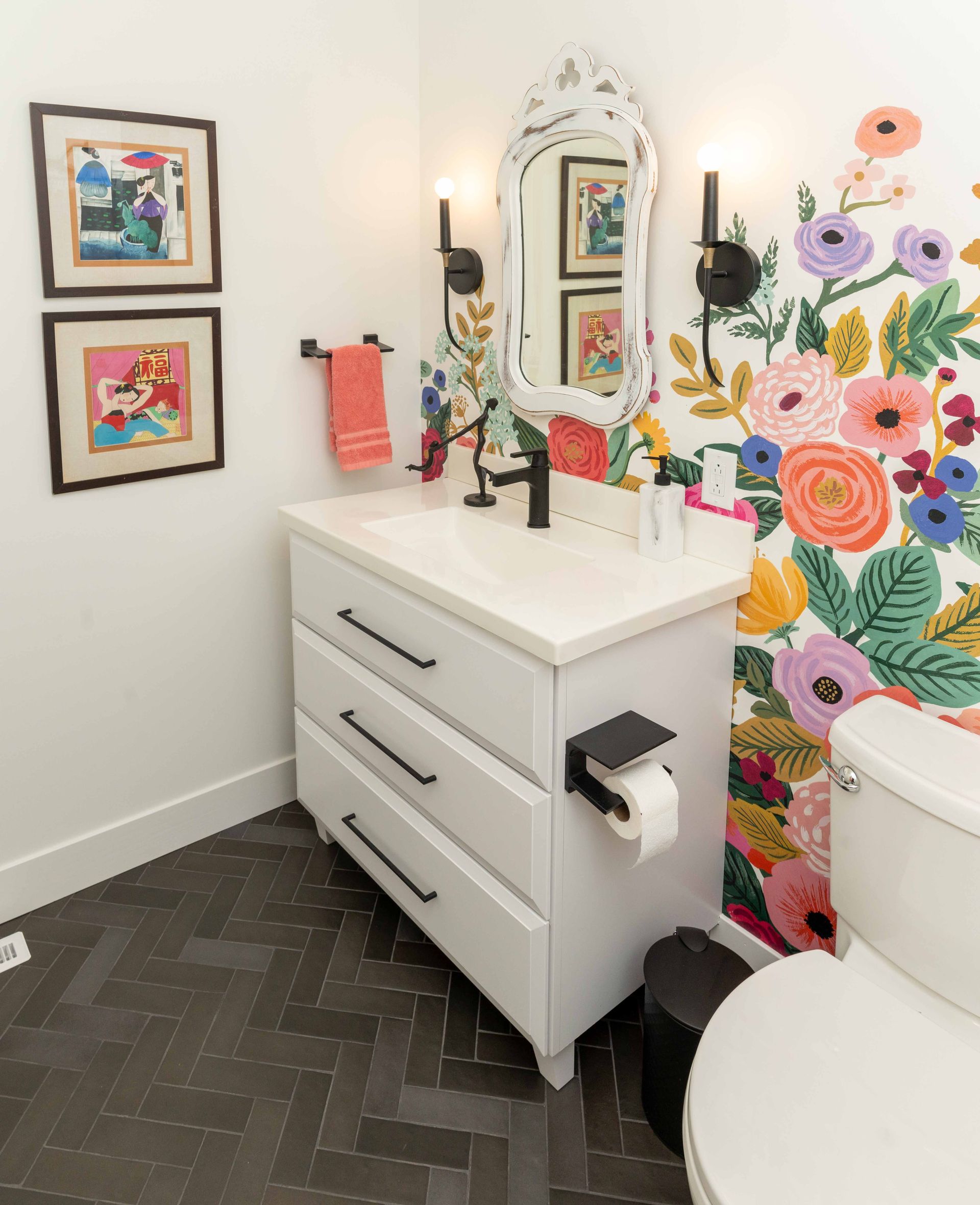 A bathroom with a toilet , sink , mirror and flowers on the wall.