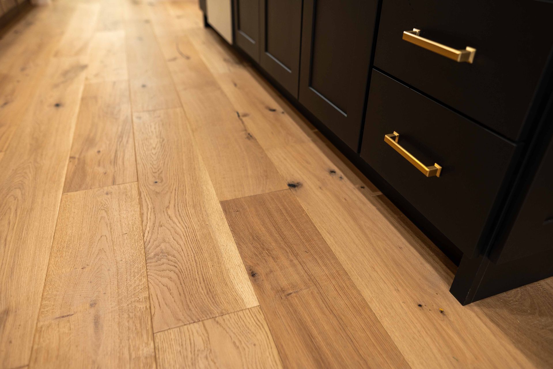 A close up of a wooden floor in a kitchen with black cabinets.