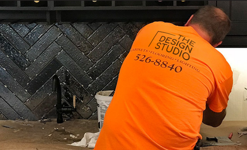 A man in an orange shirt is working on a kitchen counter.