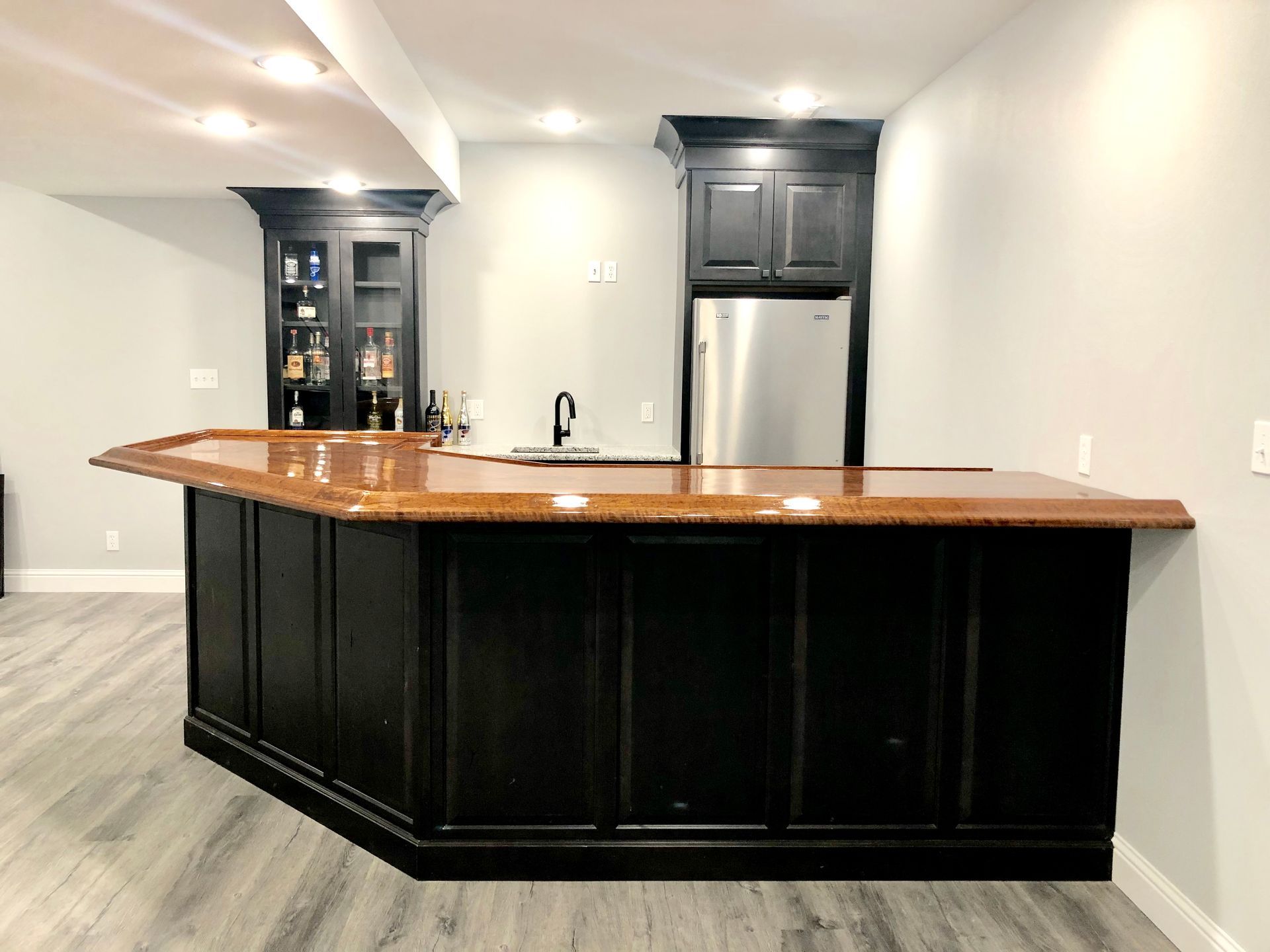 A kitchen with black cabinets and a stainless steel refrigerator