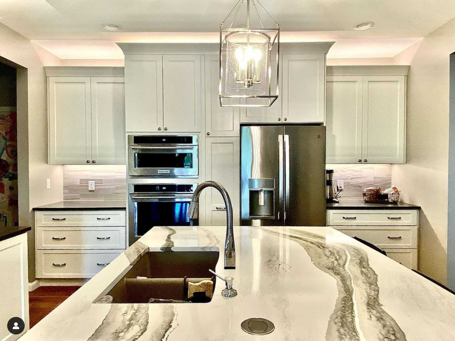 A kitchen with white cabinets , stainless steel appliances , a sink and a refrigerator.