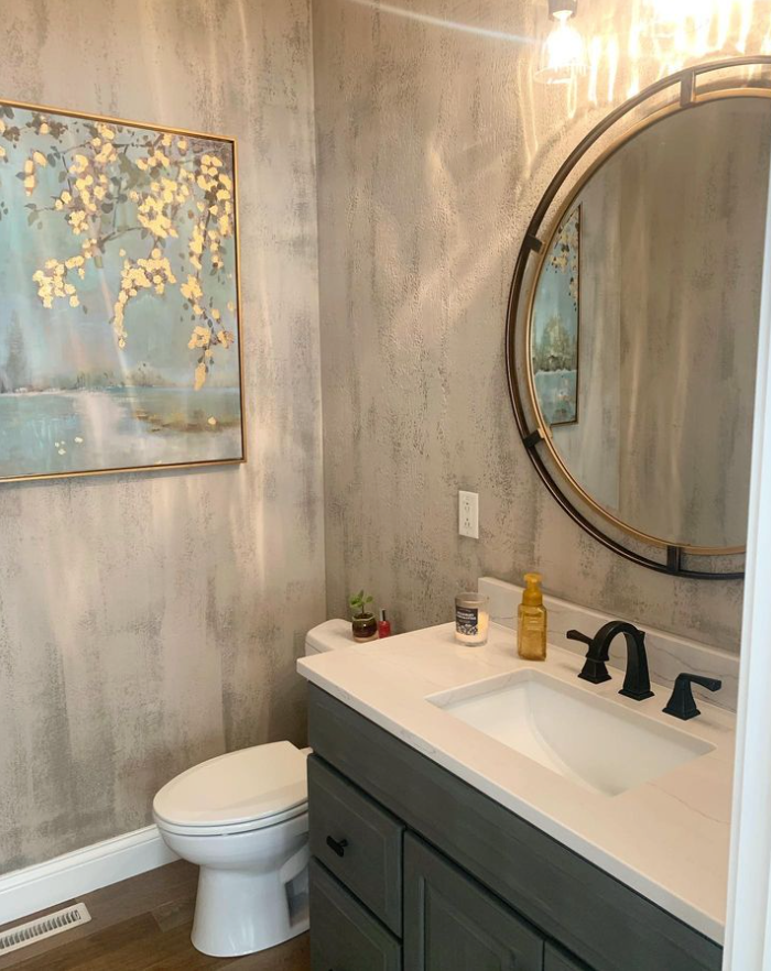 A bathroom with a toilet , sink , mirror and painting on the wall.