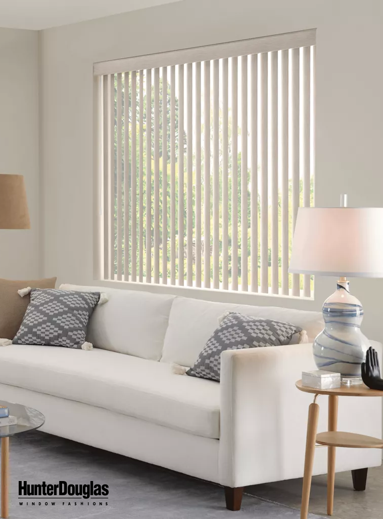 A living room with a white couch and a window with vertical blinds.