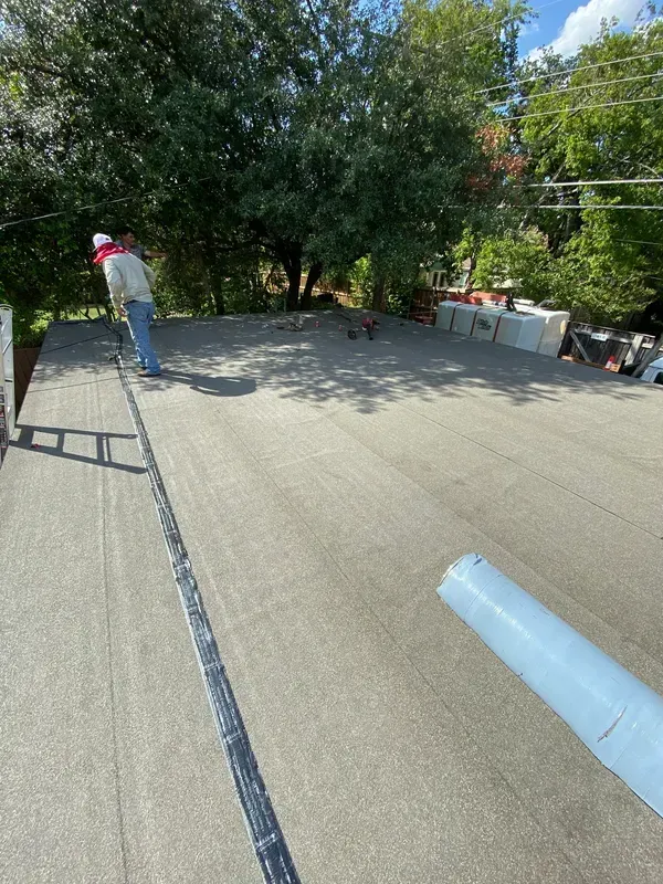 A man is standing on top of a roof with trees in the background.