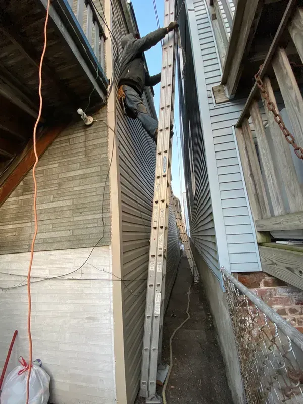 A man is standing on a ladder between two buildings.