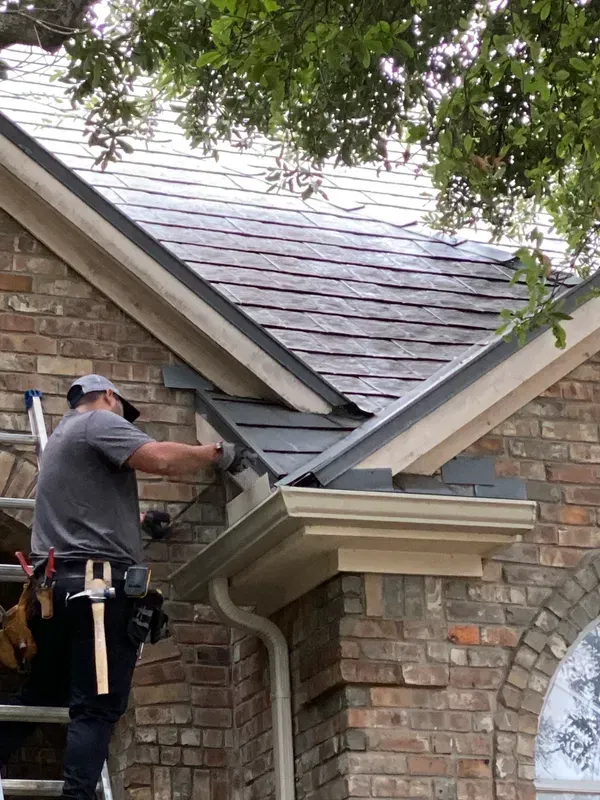 A man is working on the roof of a brick house.