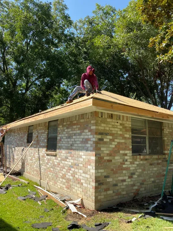 A man is sitting on the roof of a brick house.