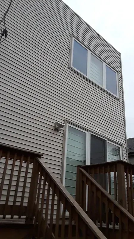 The back of a house with a wooden deck and stairs leading up to it.