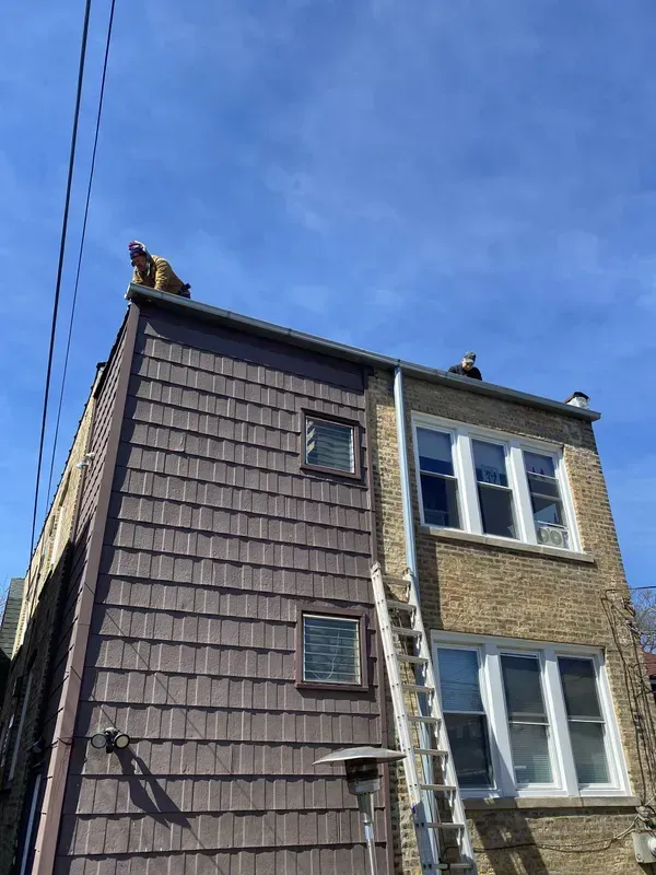 A man is standing on the roof of a building with a ladder.