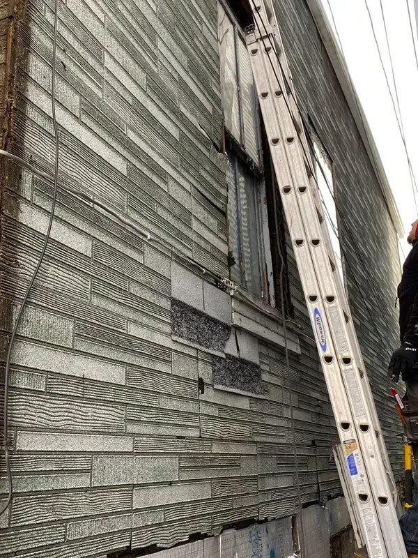 A man is standing on a ladder next to a building.