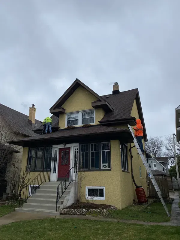 Two men are working on the roof of a yellow house.
