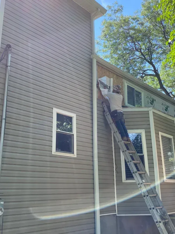 A man is standing on a ladder on the side of a house.