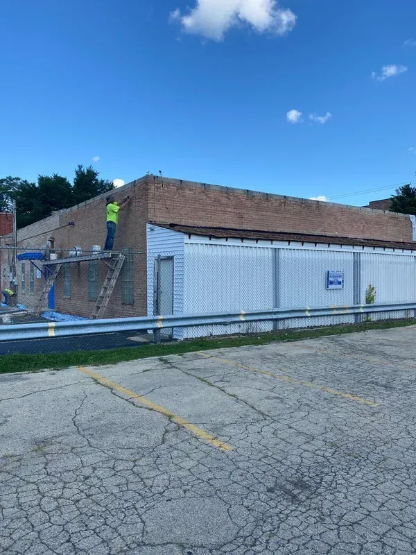A man is standing on a ladder on the roof of a building.
