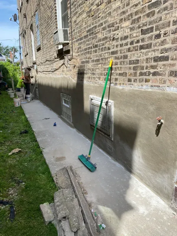 A broom is sitting on the sidewalk in front of a brick building.