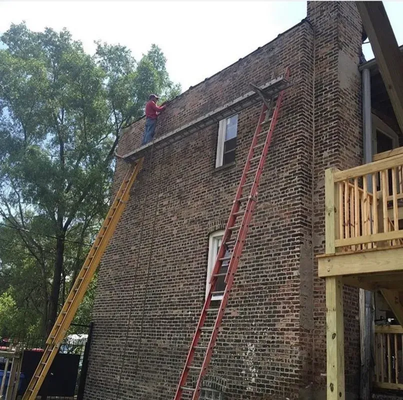 A man on a ladder is working on the side of a brick building