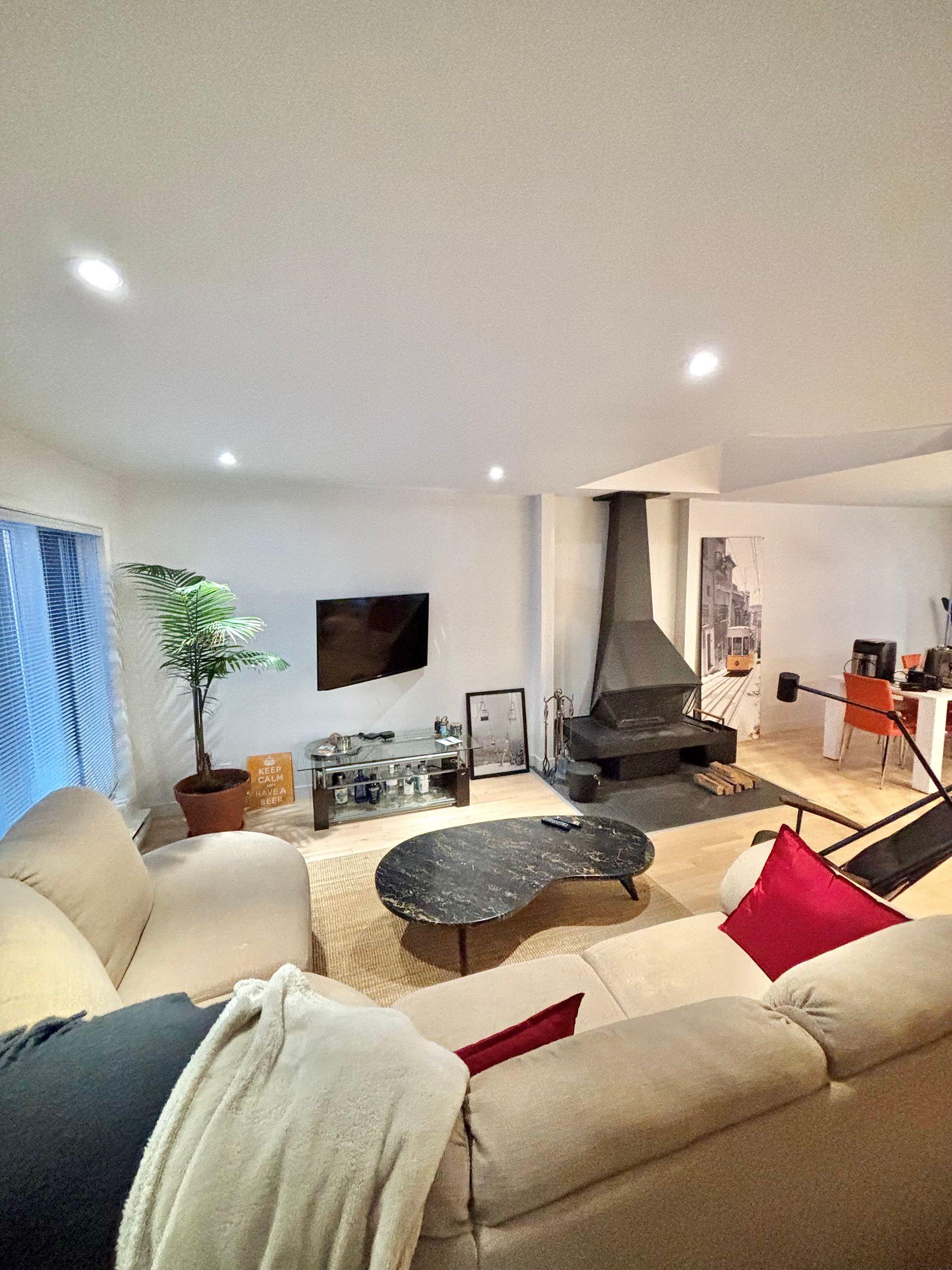 Salon spacieux avec un grand canapé d'angle, une cheminée sombre et une télévision murale. La pièce arbore une palette de couleurs neutres.