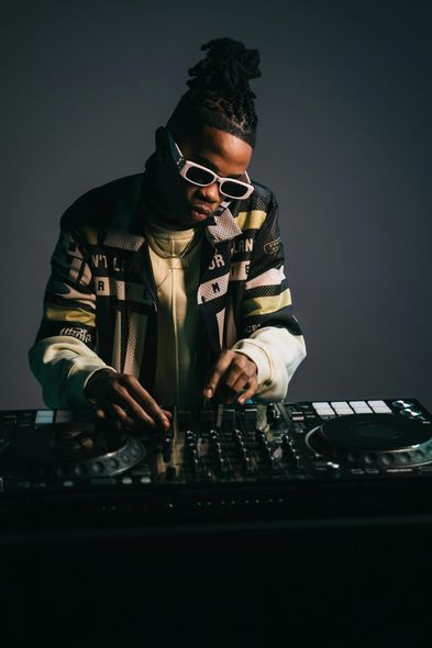 A man wearing sunglasses is playing music on a mixer.