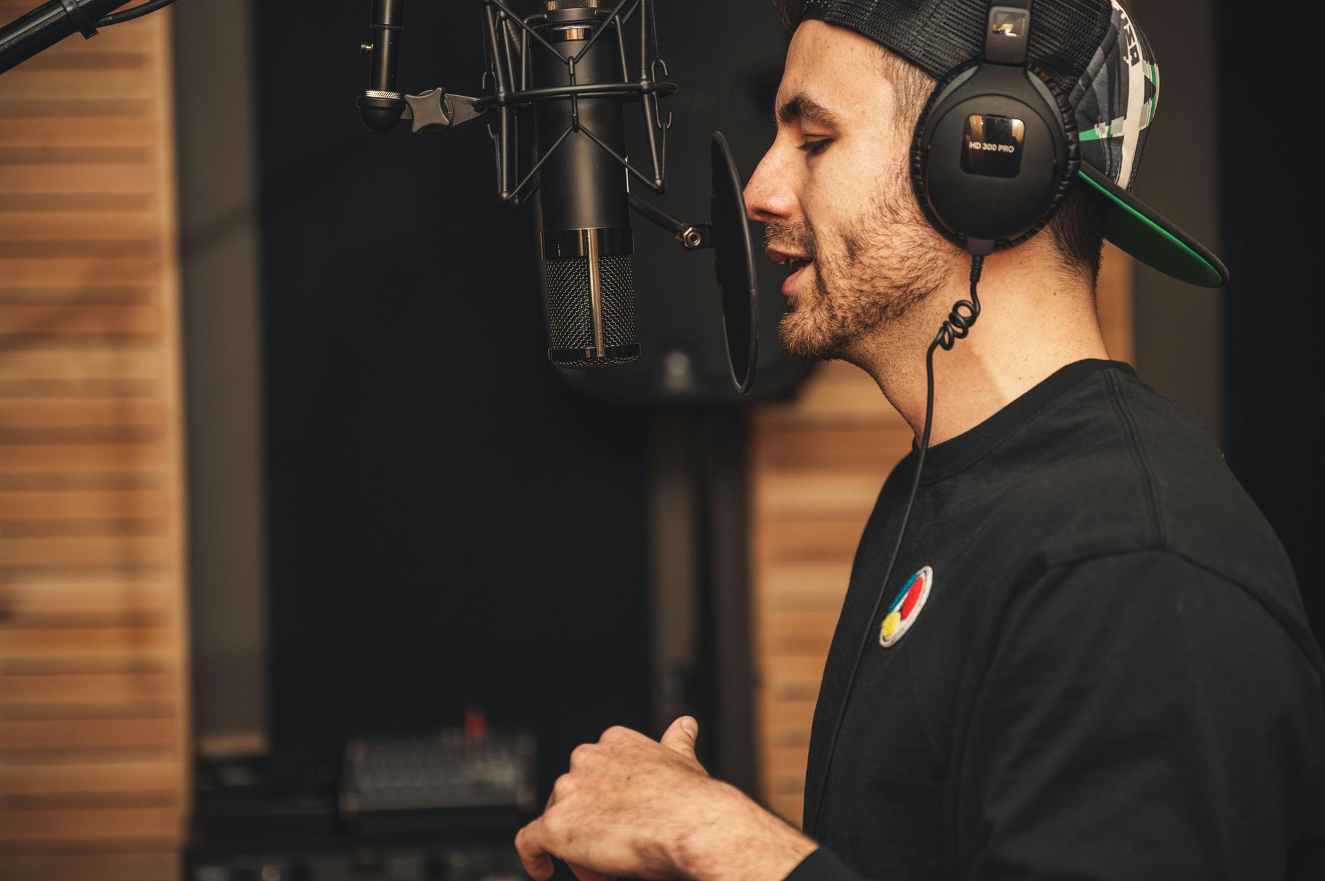 A man wearing headphones is singing into a microphone in a recording studio.