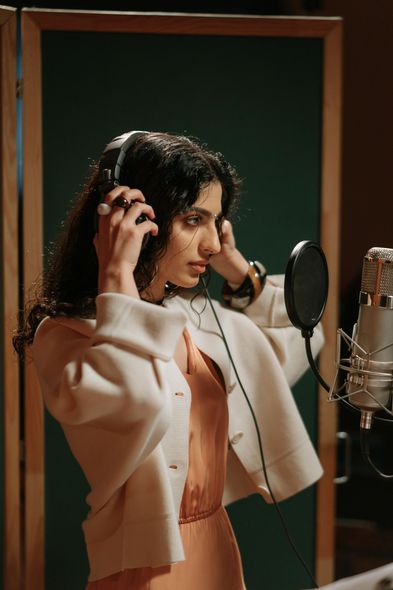 A woman is wearing headphones and singing into a microphone in a recording studio.