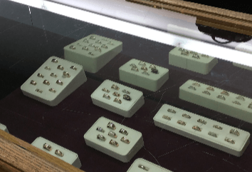 Jewelry display case with multiple white trays holding gold rings.