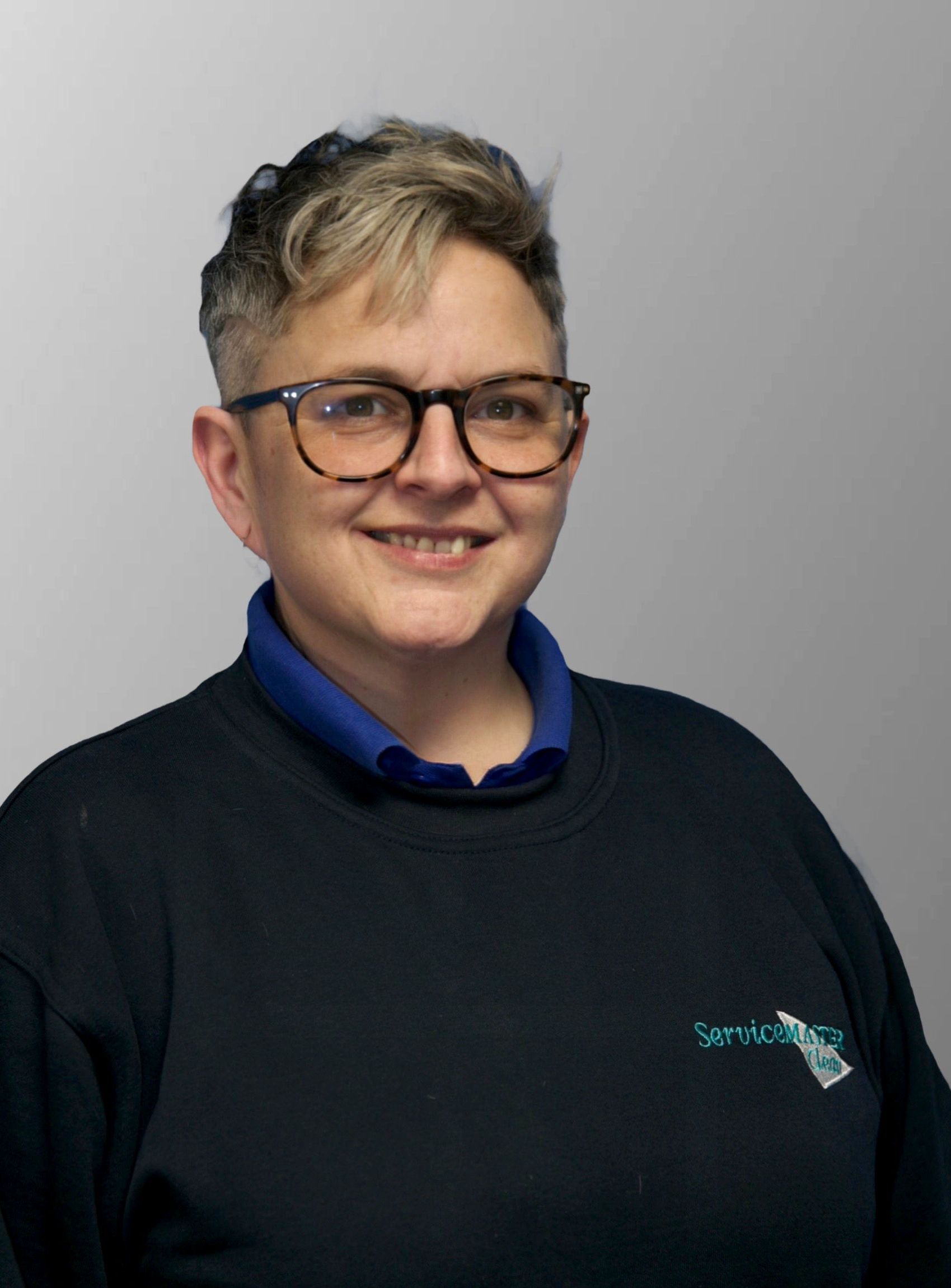 A woman in a green shirt is holding a vacuum cleaner in a hallway.