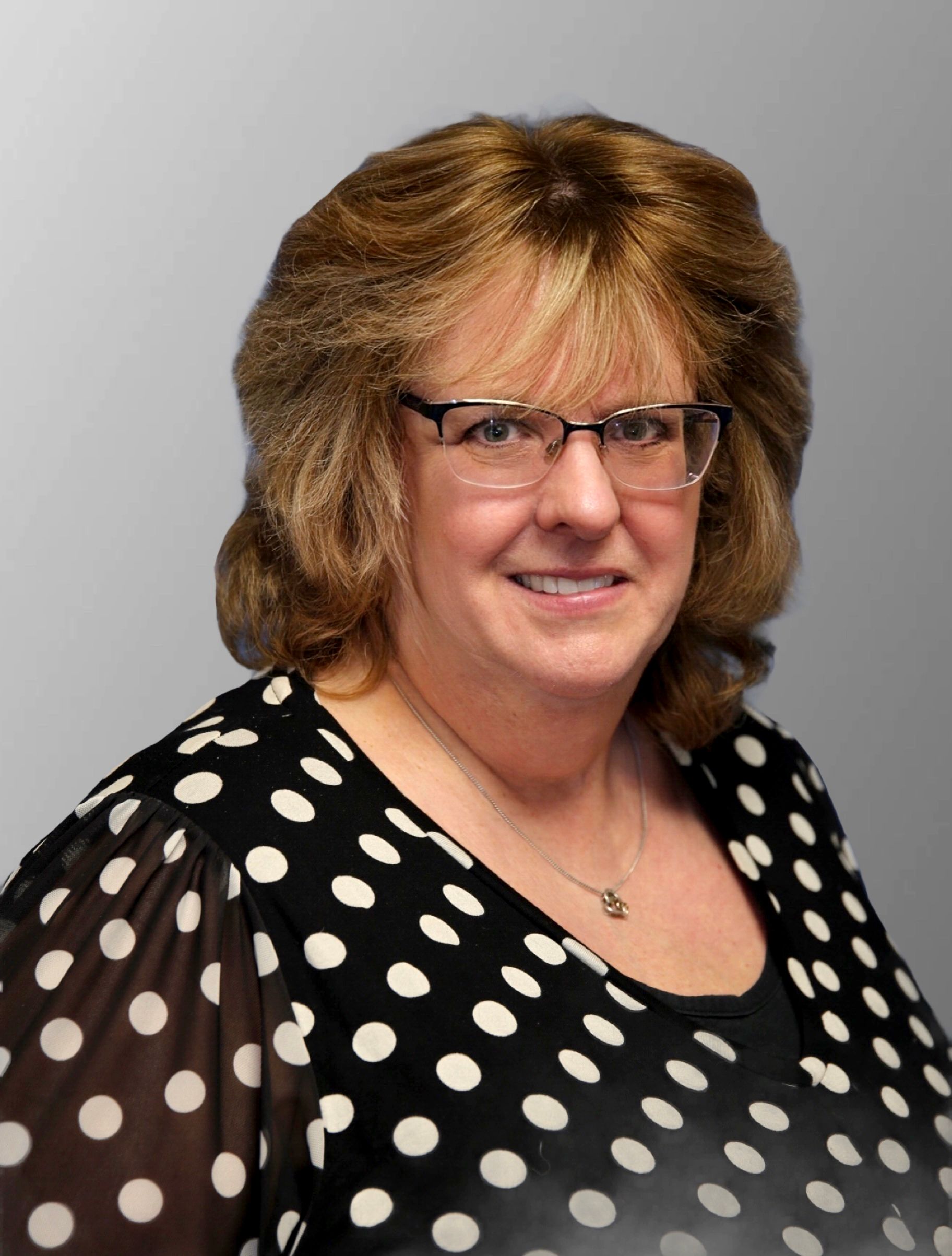 A woman wearing glasses and a black and white shirt is standing in front of a car.