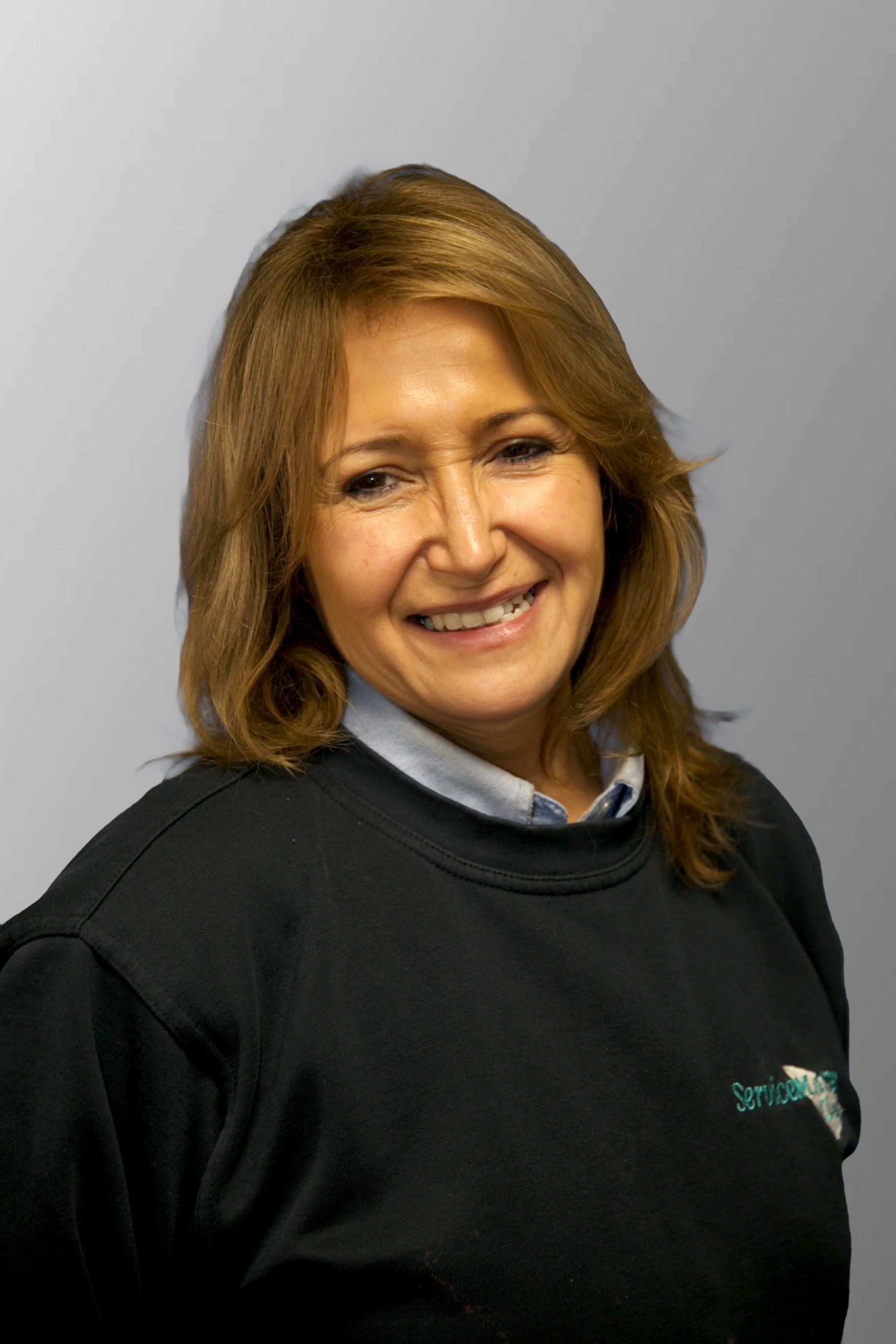 A woman wearing glasses and a blue shirt is standing in front of a yellow van.