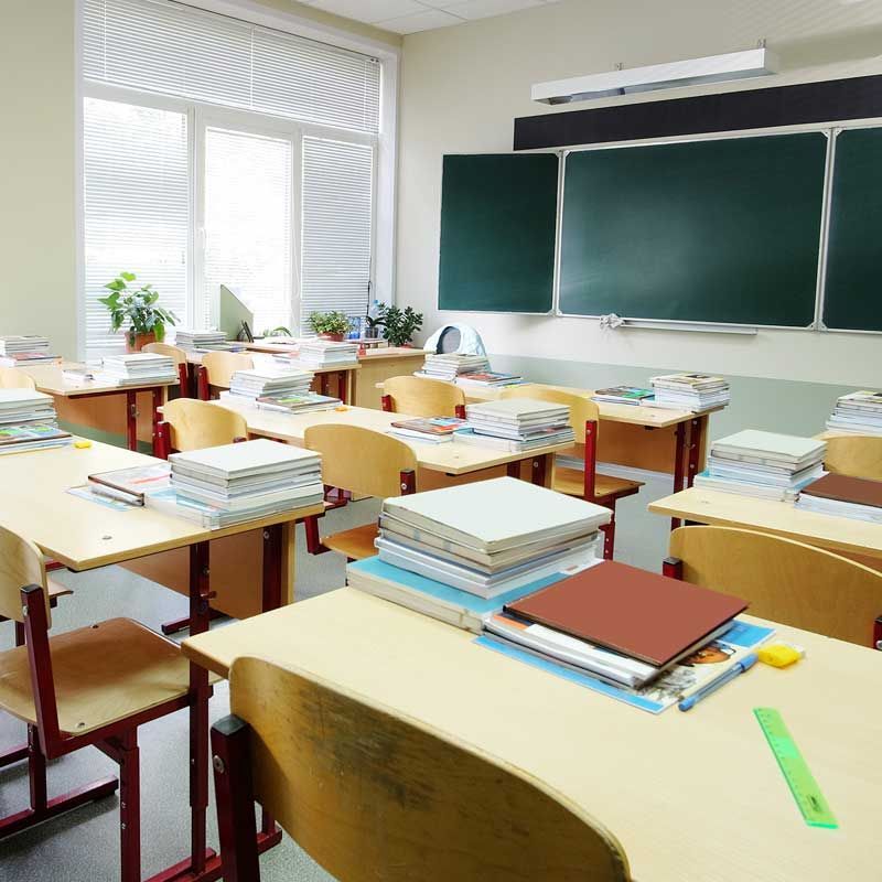 An empty classroom with lots of books on the desks