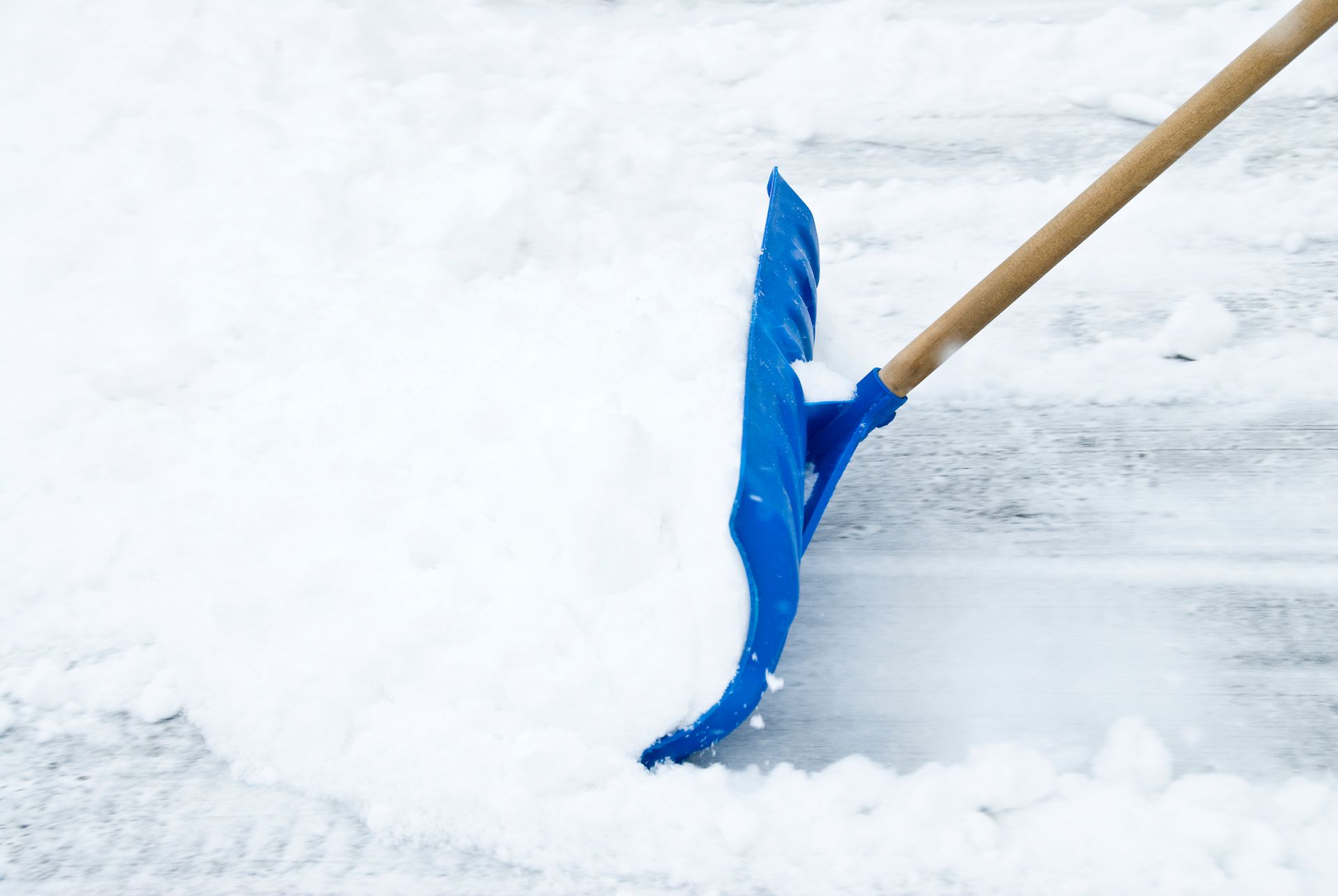 Blue snow shovel clearing snow from a pavement.